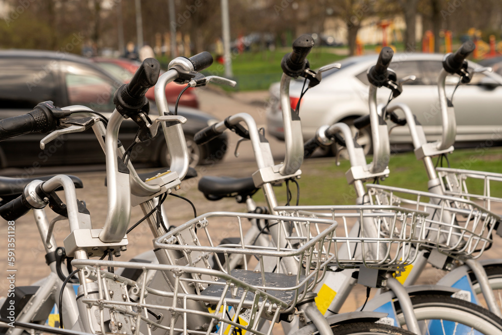 Modern rental electric bikes standing a row during charging on a bright day with a selective focus on the vertical payment terminal with a mock-up of informational or an ad banner placeholder on it