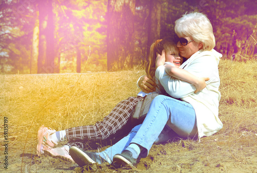 Happy grandmother with granddaughter together outdoors sitting on grass.  Happy  time. Soft sunlight and intentional soft blur foocus. Cinematic atmospheric mood photo