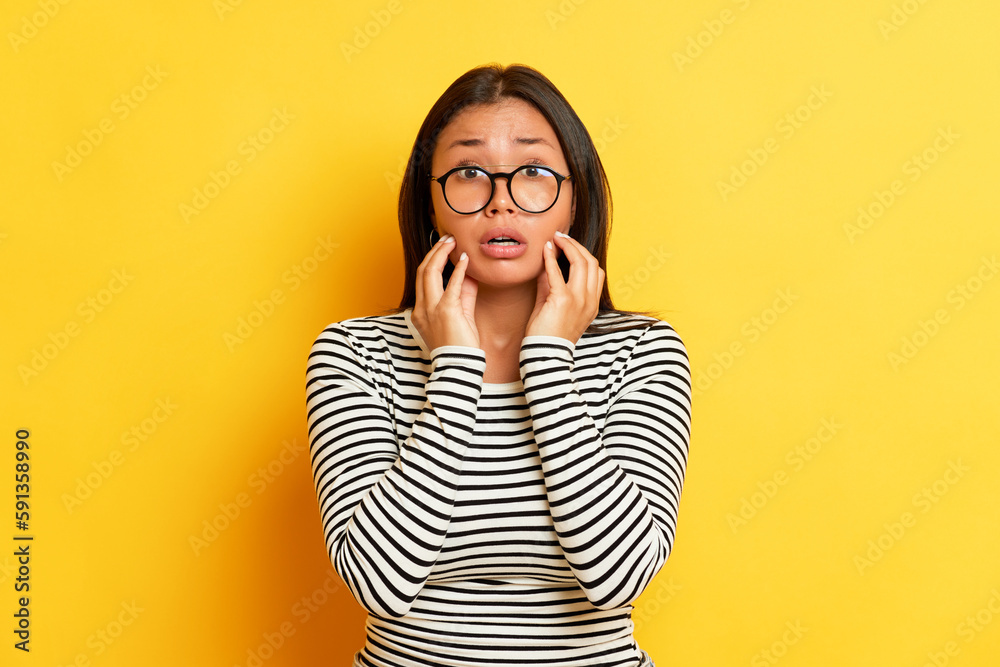 Portrait of suprised woman on yellow background, she is in black-and-white sweatshirt and holds hands up to her cheeks, copy space, high quality photo Portrait of suprised woman on yellow background, she is in black-and-white sweatshirt and holds hands up to her cheeks, copy space, high quality photo