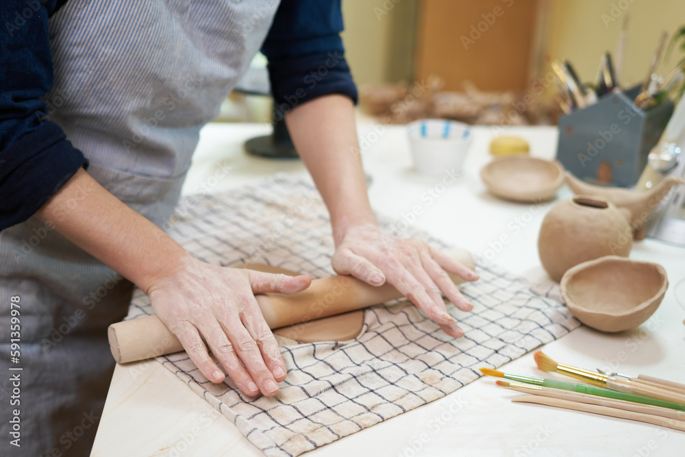 Hobbies concept - A woman ceramist rolls clay with a rolling pin in a pottery workshop