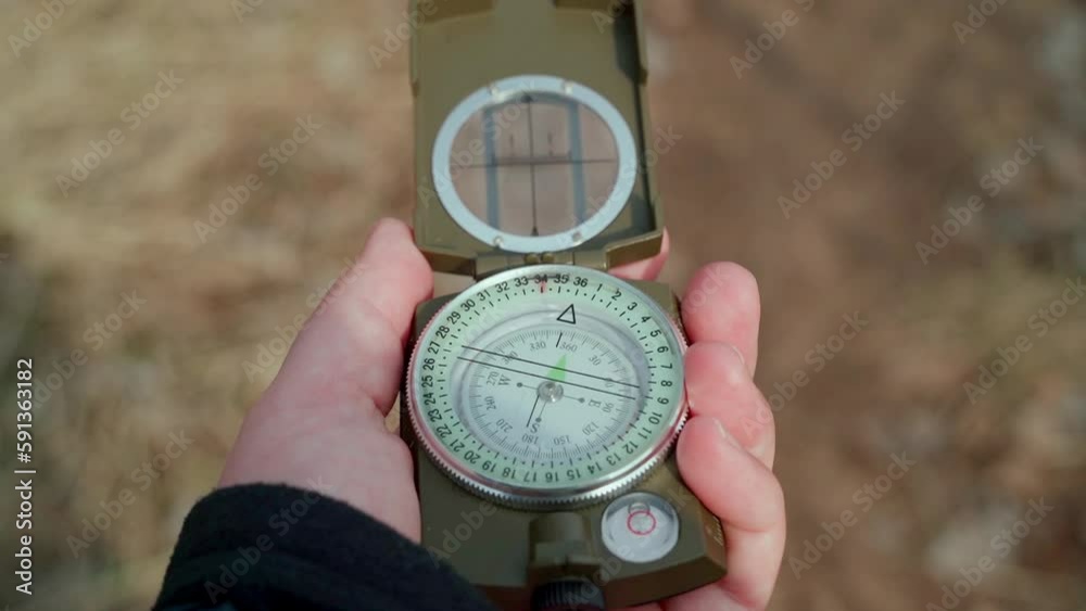 A man's hand determines the direction with a magnetic compass. The traveler uses a navigation aid while hiking. The arrow on the compass points north. Travel and active lifestyle concept. A man's hand determines the direction with a magnetic compass. The traveler uses a navigation aid while hiking. The arrow on the compass points north. Travel and active lifestyle concept.