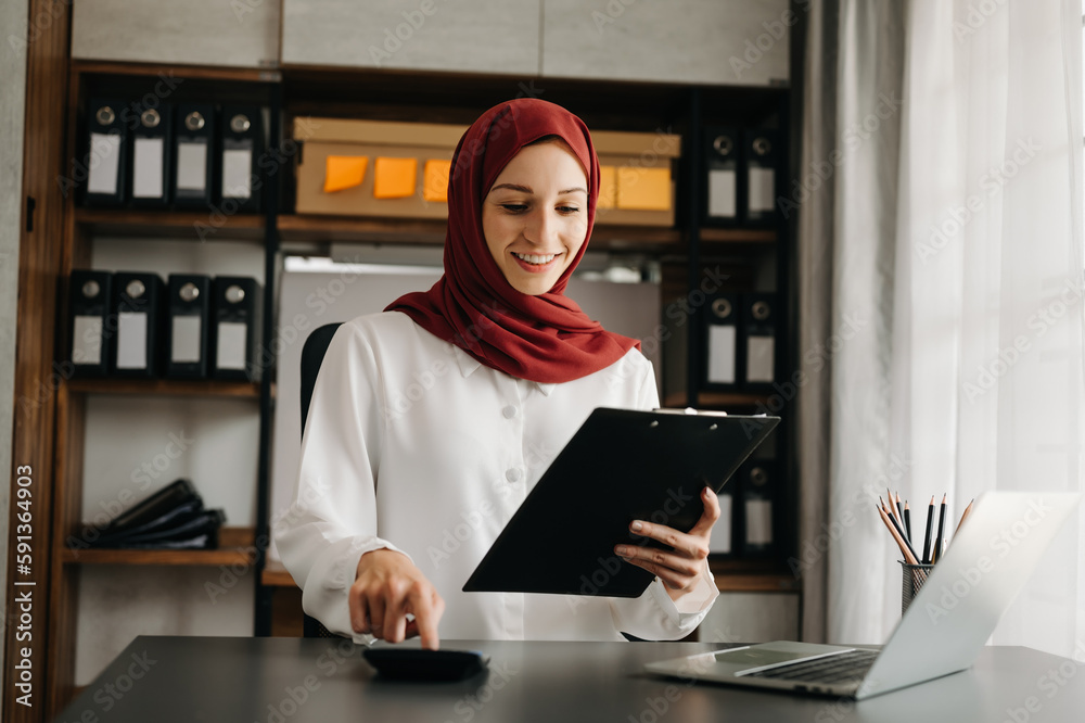 Young Arabic female entrepreneur wearing a hijab working online with a laptop at office Young Arabic female entrepreneur wearing a hijab working online with a laptop at office