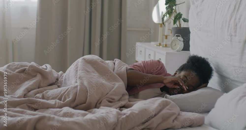 Slow motion portrait of African American lady waking up turning off alarm clock stretching arms and getting up in bedroom at home. Domestic lifestyle and people concept. Slow motion portrait of African American lady waking up turning off alarm clock stretching arms and getting up in bedroom at home. Domestic lifestyle and people concept.