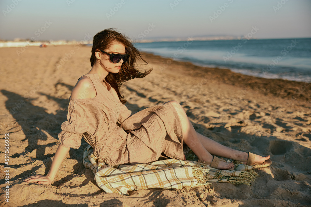 a woman in dark sunglasses sits near the sea on a blanket in windy weather a woman in dark sunglasses sits near the sea on a blanket in windy weather