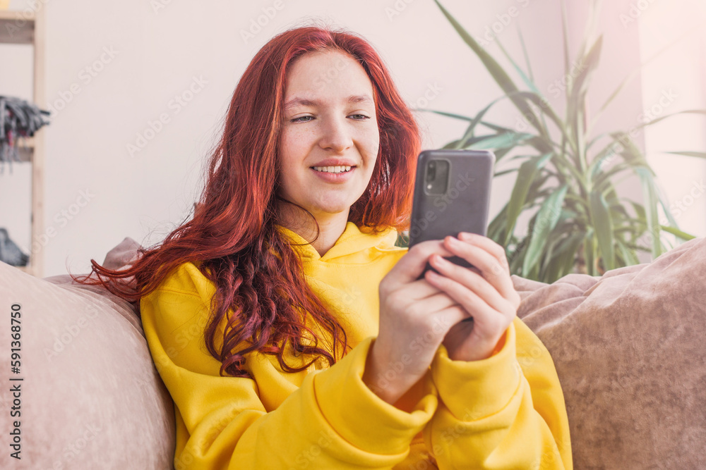 Smiling teenage girl sitting on couch and looking at phone screen Smiling teenage girl sitting on couch and looking at phone screen