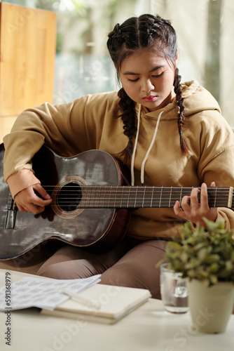 Concetrated teenage girl playing guitar at home and learning new melody