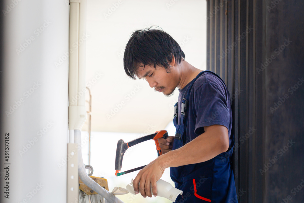 Craftsman worker sawing a pipe, Technician man installing an air conditioning in a client house, Young repairman fixing air conditioner unit, Maintenance and repairing concepts