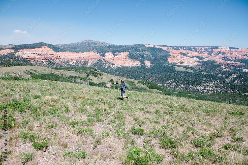 Boy running on a grassy hill with mountains in summer vacation