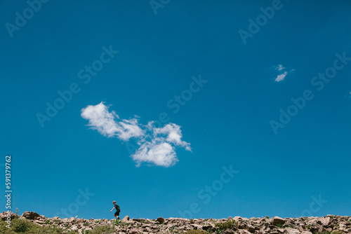 Boy walking on hike on rocky hill with blue sky in sunshine