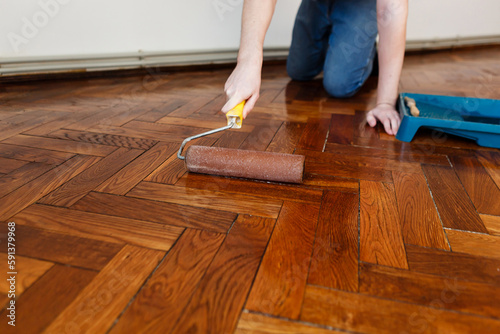 man varnishes oak parquet with a roller during renovation