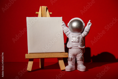 Fototapeta Naklejka Na Ścianę i Meble -  Plastic toy astronaut with paper note template mock up for your text on colorful red background Copy space. Concept of out of earth travel, private spaceman commercial flights. Space missions and