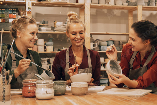 A company of three cheerful young women friends are painting ceramics in a pottery workshop.