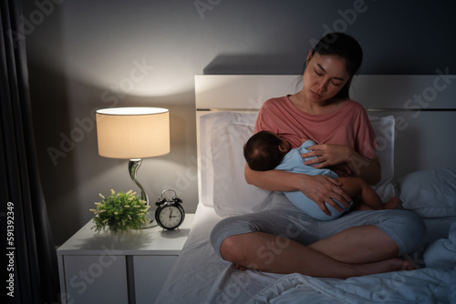 sleepy and tired mother breastfeeding newborm baby on bed at night