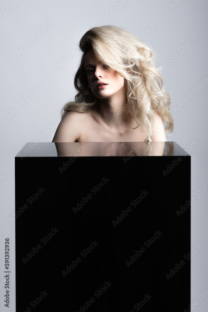 Beauty, fashion and make-up concept. Beautiful sexy blonde woman with big wavy hair holding hands on black glass cube with copy space. Minimalistic and futuristic looking style Beauty, fashion and make-up concept. Beautiful sexy blonde woman with big wavy hair holding hands on black glass cube with copy space. Minimalistic and futuristic looking style