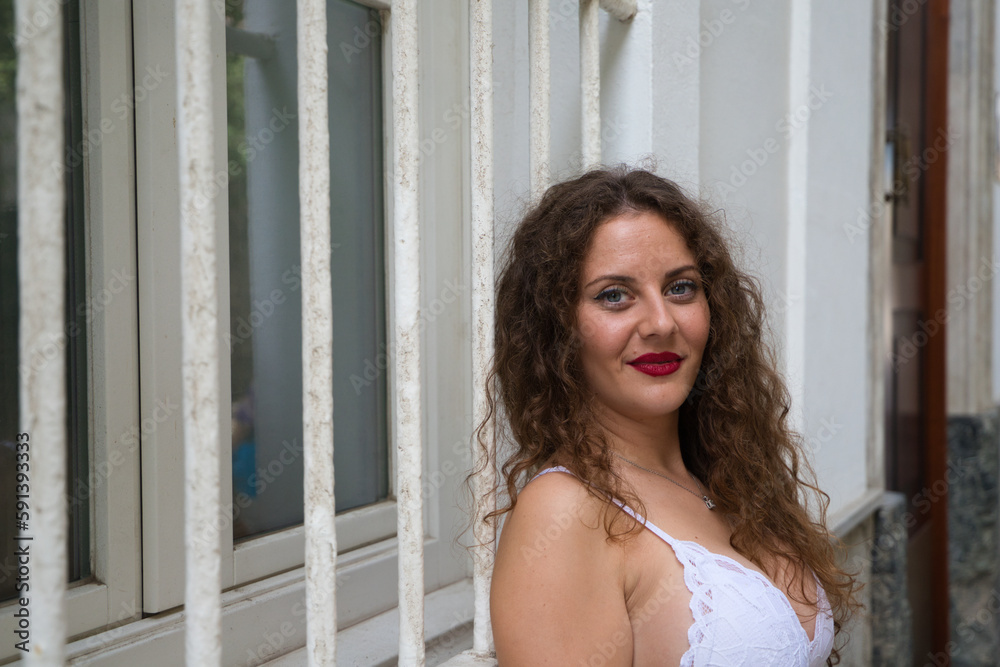 Beautiful woman, young and blonde with curly hair and blue eyes leaning against a wall on the street poses for photos in a sensual way looking at the camera. The woman is on vacation in Spain, Europe. Beautiful woman, young and blonde with curly hair and blue eyes leaning against a wall on the street poses for photos in a sensual way looking at the camera. The woman is on vacation in Spain, Europe.
