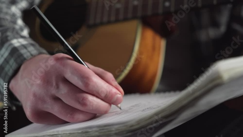 young man writing song lyrics with acoustic guitar in cozy room. close-up.