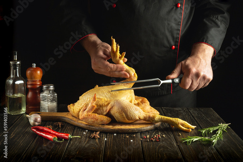 Dish of fried chicken by the hands of the cook in the kitchen of the restaurant. Preparing to cook a raw rooster on a cutting board. Fork in the chef hand.