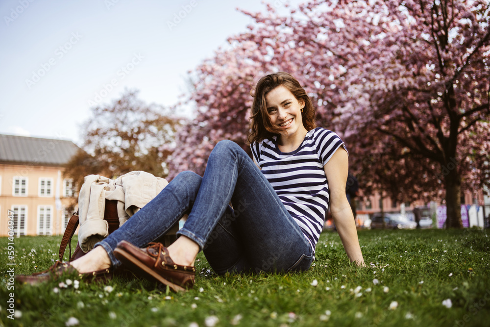 Young woman sitting on a spring meadow in the park and laughing at the camera