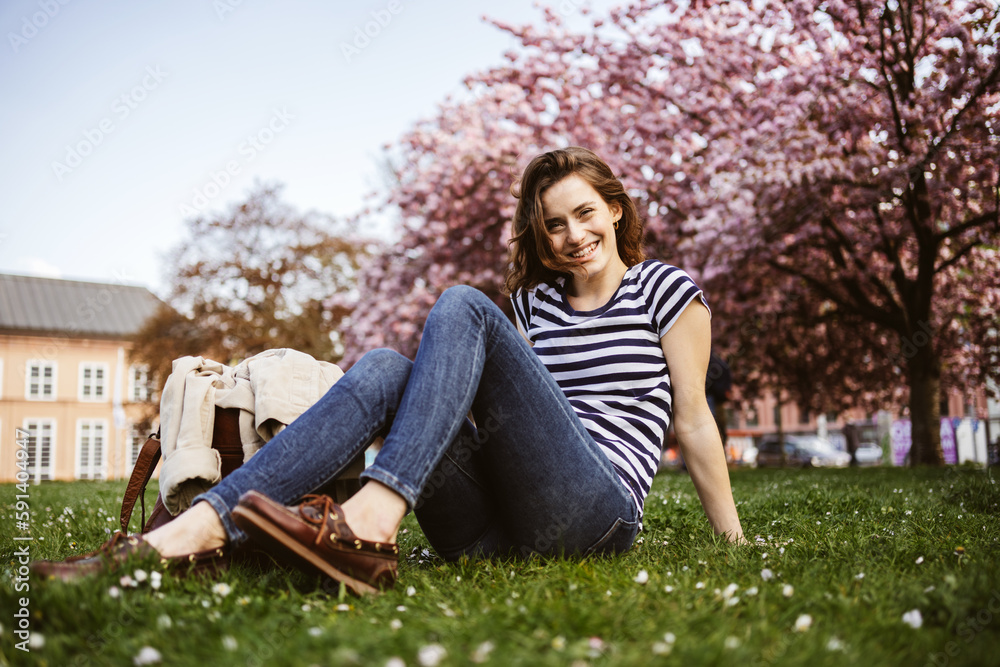Young woman sitting on a spring meadow in the park and laughing at the camera Young woman sitting on a spring meadow in the park and laughing at the camera