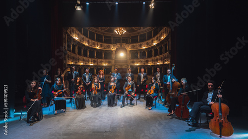Group Photo: Portrait of Symphony Orchestra Performers on the Stage of a Classic Theatre, Looking at the Camera Together and Smiling. Successful and Professional Musicians Posing  photo
