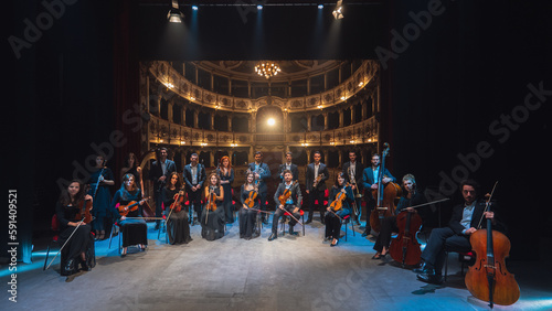 Group Photo: Portrait of Symphony Orchestra Performers on the Stage of a Classic Theatre, Looking at the Camera Together and Smiling. Successful and Professional Musicians Posing