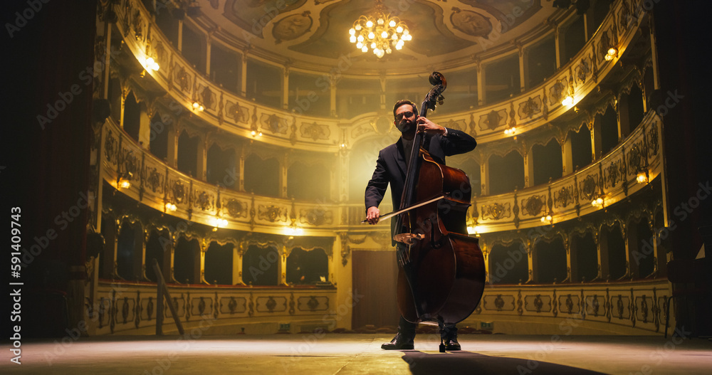 Cinematic shot of Male Cellist Playing Cello Solo on an Empty Classic Theatre Stage with Dramatic Lighting. Professional Musician Rehearsing Before the Start of a Big Show with Orchestra