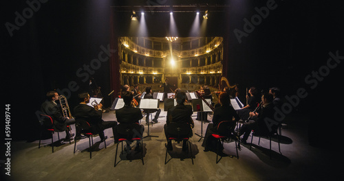 Wide Cinematic shot of Conductor Directing Symphony Orchestra with Performers Playing Violins, Cello and Trumpet on Classic Theatre with Curtain Stage During Music Concert. Back View