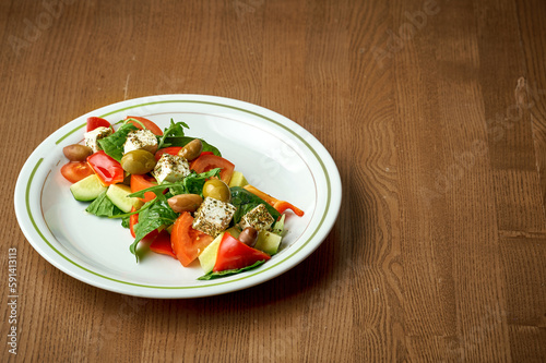Greek salad with olives, feta cheese and vegetables in a plate on a wooden background