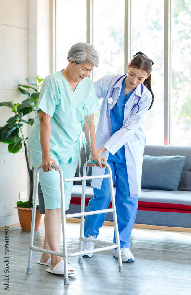 Asian young professional successful friendly female nurse in blue hospital uniform helping supporting physical therapy senior old pensioner unhealthy injury woman patient walking via four legs walker Asian young professional successful friendly female nurse in blue hospital uniform helping supporting physical therapy senior old pensioner unhealthy injury woman patient walking via four legs walker