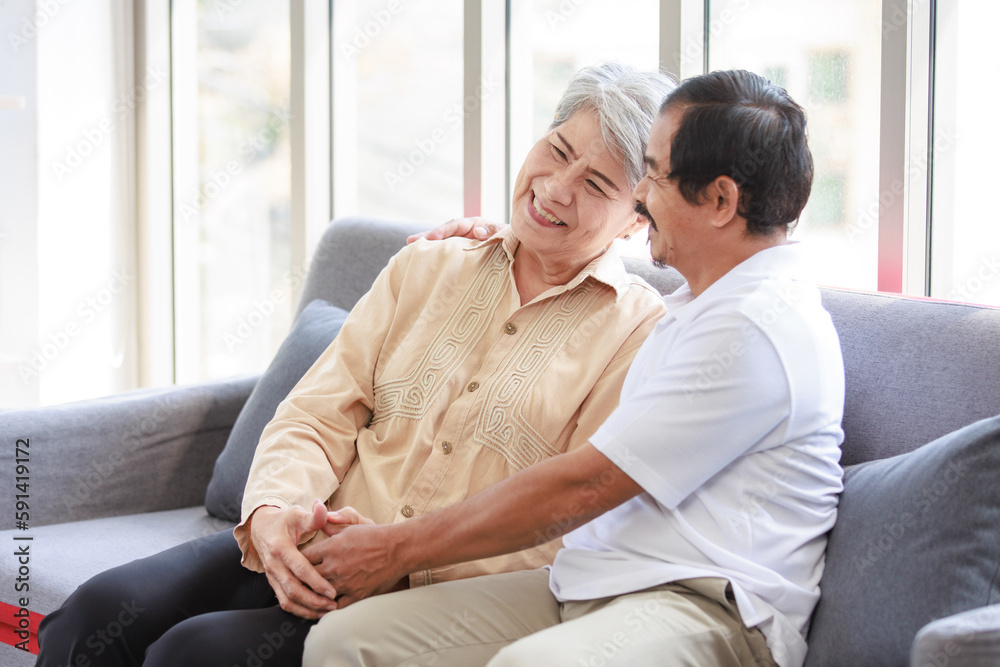 Asian old senior elderly pensioner aged lovely couple male female husband and wife sitting on cozy sofa couch holding each other hands smiling talking discussing supporting together in living room Asian old senior elderly pensioner aged lovely couple male female husband and wife sitting on cozy sofa couch holding each other hands smiling talking discussing supporting together in living room