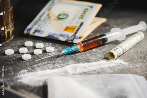 Syringe with a dose of drugs, white pills, powder narcotics, and US dollar currency on dark background. Concept of addiction, abuse and bad habits