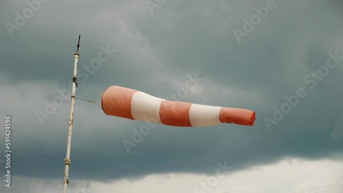 A white and red windsock on a windy day, mounted on a pipe with peeling paint. Against a dark sky with a huge cloud. Close-up. Slow motion