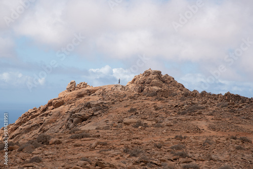 Hombre caminando sobre una ladera rocosa y montañosa en medio de un paisaje desértico en un día soleado con cielo nublado en las Islas Canarias de Fuerteventura. photo