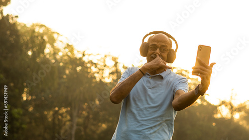 Happy senior citizen man in park listening music in headphones