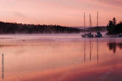 Scenic shot of boats and their reflection on the surface of a lake at a pink sunset