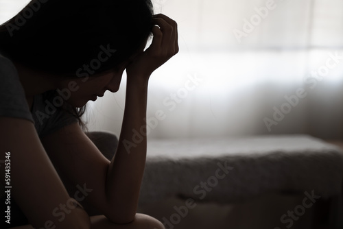 Depressed woman sitting alone on the bed with hands on head feel stress, sad and worried in the dark bedroom and low light environment