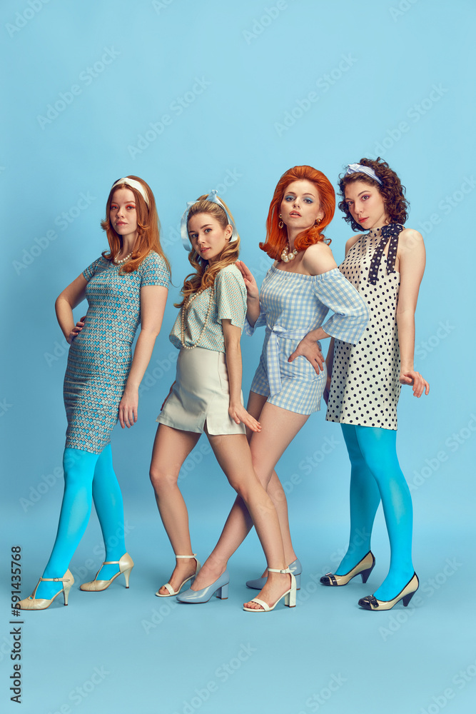 Fototapeta premium Fashion show. Full-length portrait of beautiful young women posing in stylish clothes against blue studio background. Concept of retro style, fashion, beauty, elegance, 60s, youth. Pin-up style