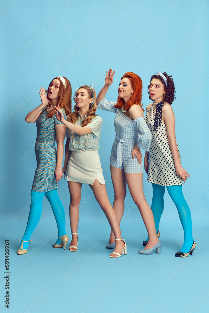 Greetings. Full-length portrait of beautiful young women posing in stylish clothes against blue studio background. Concept of retro style, fashion, beauty, elegance, 60s, youth. Pin-up style