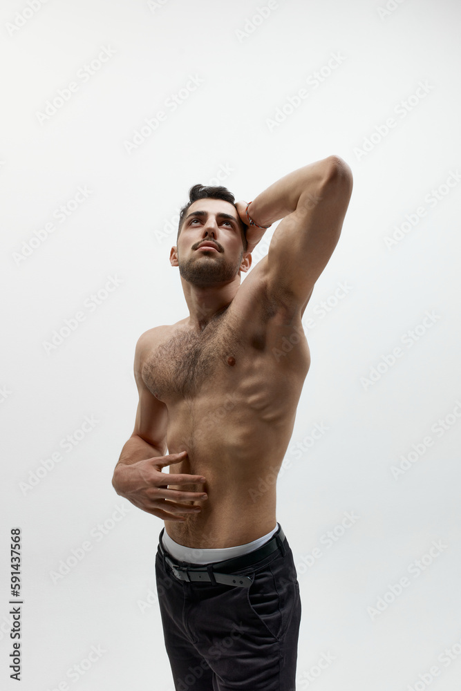 Portrait of pensive young muscular man standing shirtless and looking up over white studio background. Naked torso Portrait of pensive young muscular man standing shirtless and looking up over white studio background. Naked torso