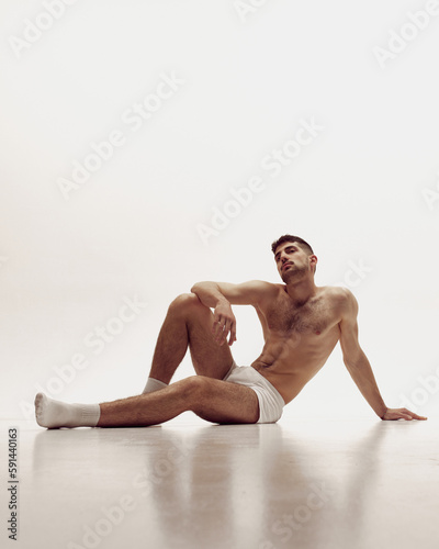 Handsome young muscular man posing shirtless over light studio background. Aesthetics of male body