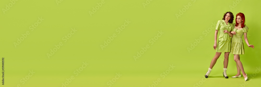 Portrait of two pretty young woman with stylish hairdo emotionally posing against green studio background. Retro style, fashion, beauty, elegance, 60s concept. Pin-up style. Banner. Copy space for ad Portrait of two pretty young woman with stylish hairdo emotionally posing against green studio background. Retro style, fashion, beauty, elegance, 60s concept. Pin-up style. Banner. Copy space for ad