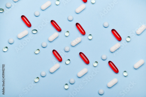 Flat lay with red gel translucent capsules with Omega or fish oil, gelatin dragees with fat soluble vitamin D and medical pills arranged in pattern on isolated blue backdrop. Pharma business. Industry