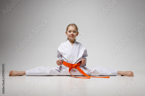 A little girl in a white kimono with an orange belt sits on a twine.