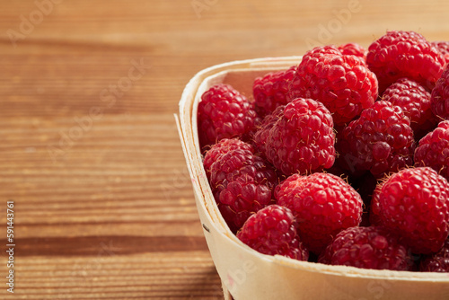 delicious fresh raw red raspberries in natural eco-friendly packaging in a basket of peeled hardwood veneer on a wooden table closeup. harvest. healthy food. diet. summer. vitamins