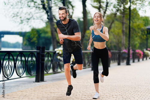 Morning jogging. Wide image of happy smiling young couple, runners running together, woman train with man, or bearded fit coach exercising outdoors. Fitness, sport city marathon workout concept.