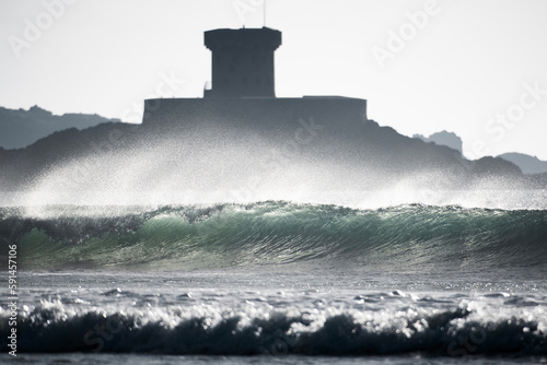 A backlit wave with La Rocco Tower in the background photo