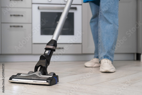 Close-up of a woman holding a vertical vacuum cleaner in her hands while cleaning in a modern kitchen. Employee of a cleaning company or a housewife cleans the house.