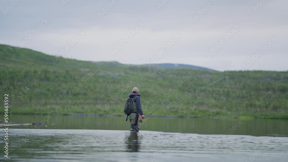 Wide view of man with fishing gear walking in water at Swedish lake Wide view of man with fishing gear walking in water at Swedish lake