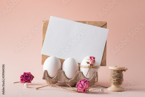 A mock-up of an invitation with Easter eggs and an eco-decor of dried roses and a wooden rabbit on a beige background.