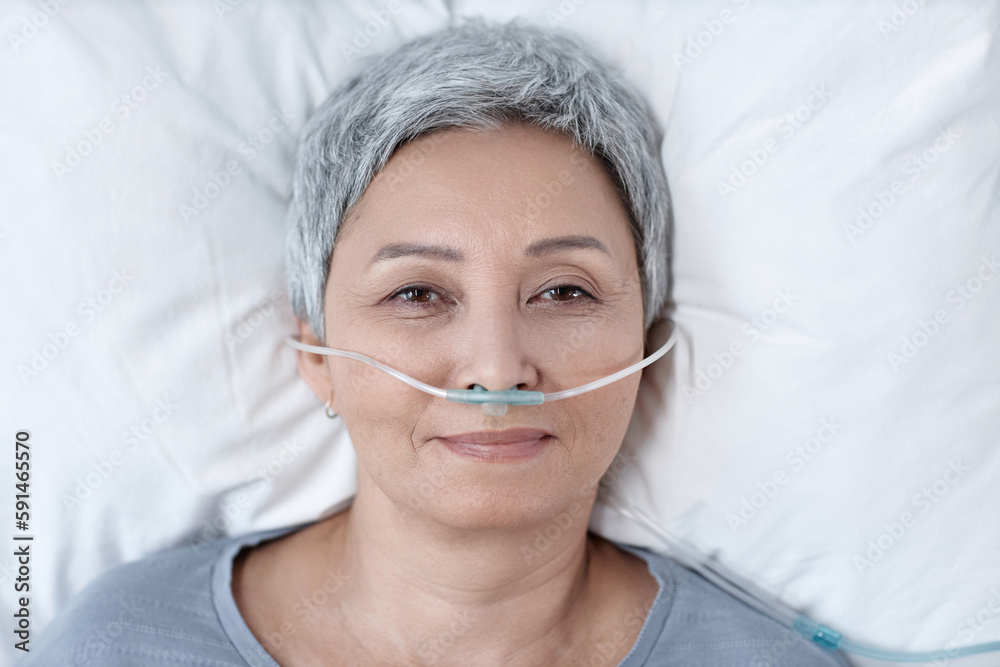 High angle view of senior woman in oxygen tube in her nose looking at camera while lying on bed in ward High angle view of senior woman in oxygen tube in her nose looking at camera while lying on bed in ward
